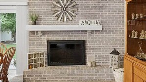 A fireplace with a brick wall, a shelf above it, and a word 'FAMILY' on the wall. - Poolside Pokes...Walk to OSU!!! (Stillwater)