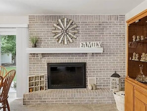A fireplace with a brick wall, a shelf above it, and a word 'FAMILY' on the wall. - Poolside Pokes...Walk to OSU!!! (Stillwater)