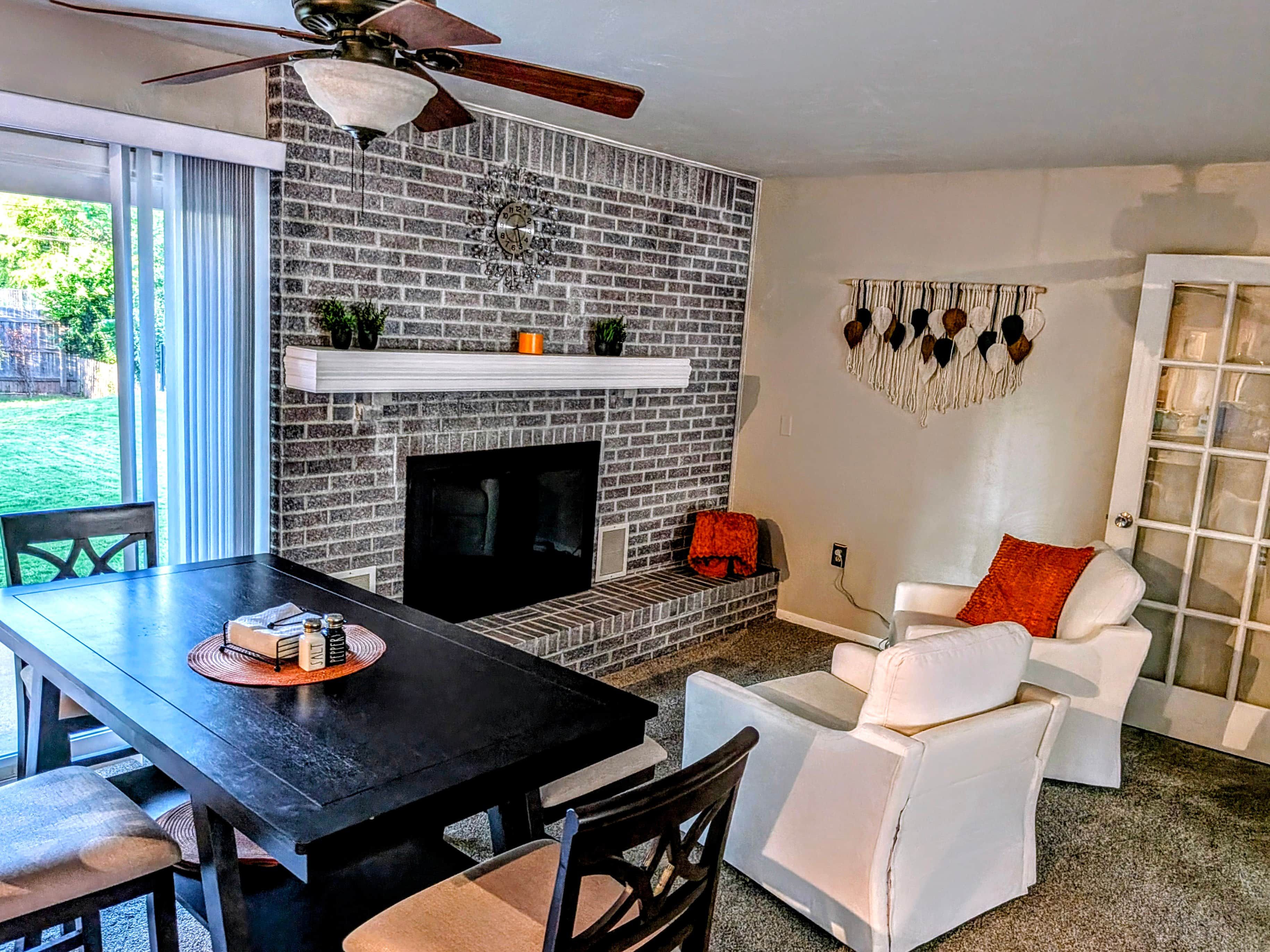 A living room with a brick fireplace, a ceiling fan, a white sofa, and a dining table.