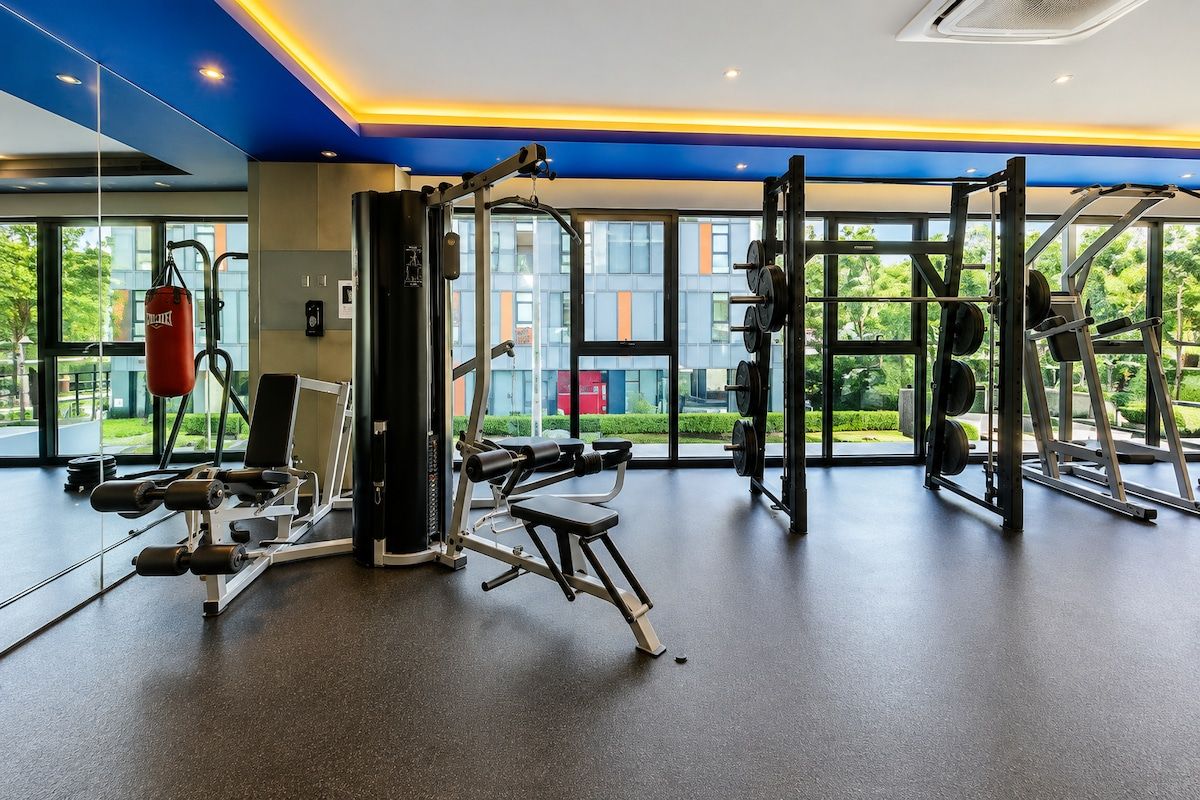 A gym with various exercise equipment, large windows, and a view of greenery outside.