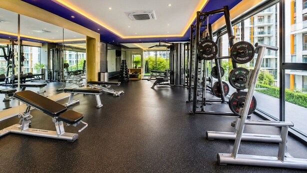 Un gimnasio con equipamiento de levantamiento de pesas, bancos y un muro de espejos.