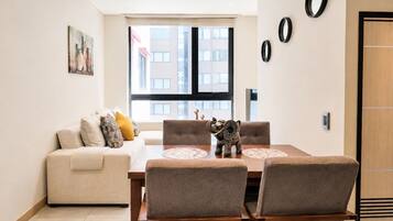 A dining area with a table and chairs, a sofa, and a window with a view of buildings.