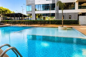 En swimmingpool med en modern byggnad i bakgrunden, ett överbyggt sittområde och en palm.