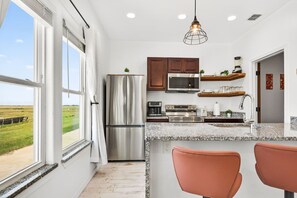 A modern kitchen with stainless steel appliances, granite countertops, and a view of the countryside. - Luxe 4BR: Boardwalk + 3rd Floor Deck (Port Aransas)