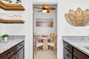 A kitchen with granite countertops, wooden cabinets, a dining table with chairs, a ceiling fan, and a wall-mounted decorative piece. - Luxe 4BR: Boardwalk + 3rd Floor Deck (Port Aransas)