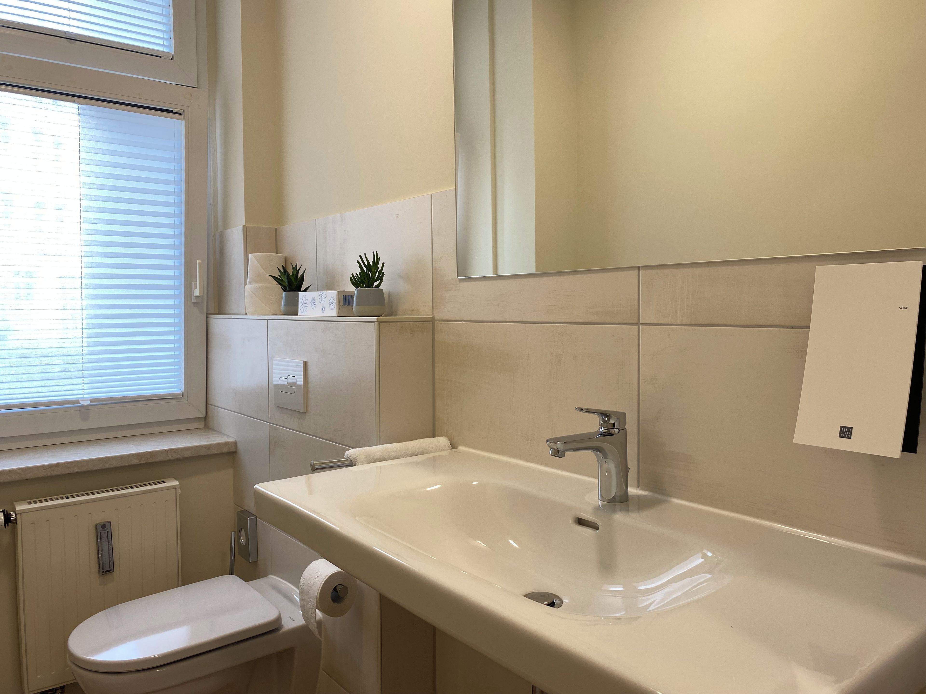 A bathroom with a toilet, sink, and window with blinds.