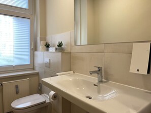 A bathroom with a toilet, sink, and window with blinds. - Alte Gärtnerei 1: Helle Ferienwohnung zentral in Bautzen (Bautzen)