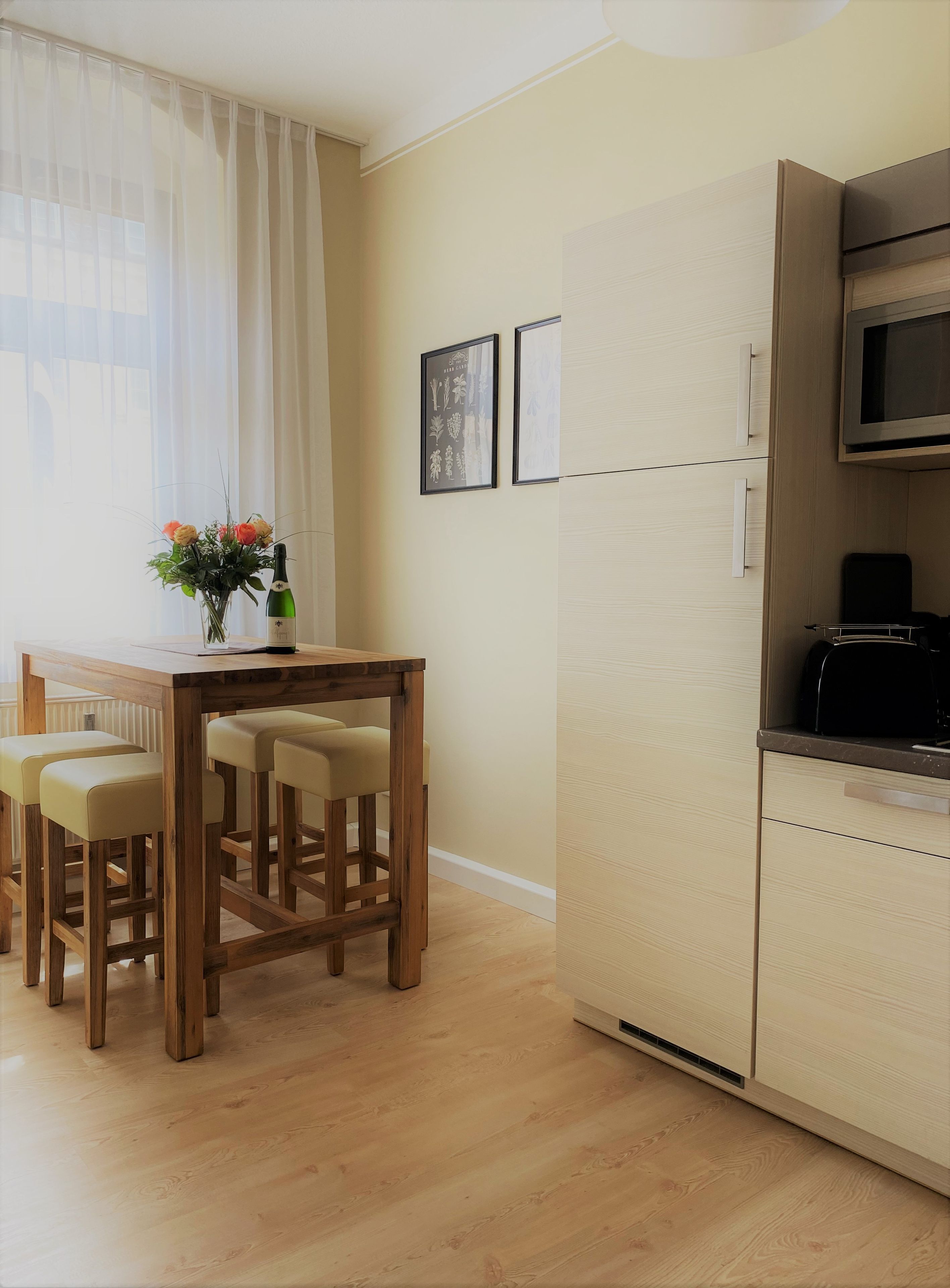 A modern kitchen with a built-in microwave, a wooden dining table with four chairs, and a vase with flowers on the window sill.