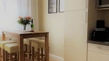 A modern kitchen with a built-in microwave, a wooden dining table with four chairs, and a vase with flowers on the window sill.