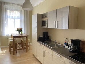 A modern kitchen with wooden cabinets, a stainless steel microwave, a coffee maker, and a sink. - Alte Gärtnerei 1: Helle Ferienwohnung zentral in Bautzen (Bautzen)