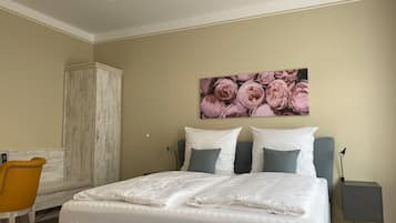 A bedroom with a bed, a nightstand, a chair, a wardrobe, and a floral artwork on the wall.
