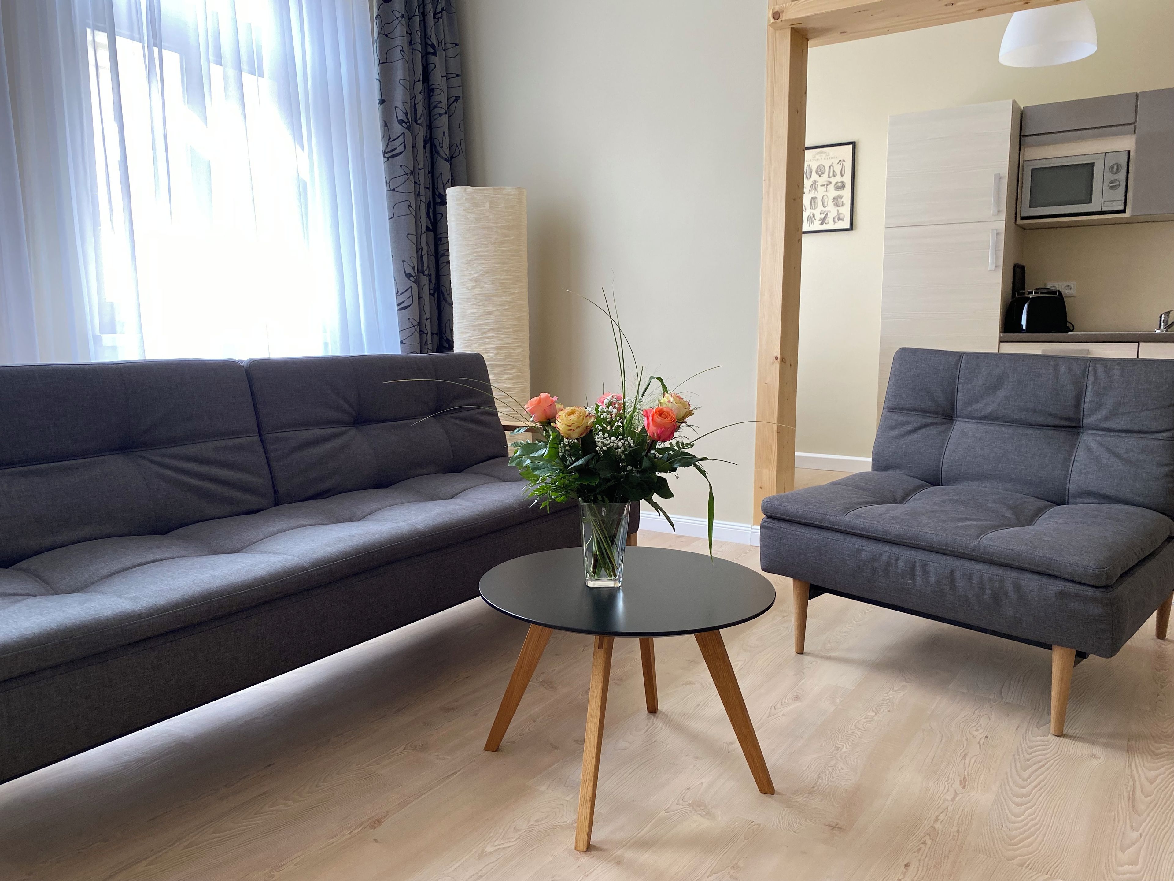 Een woonkamer met een grijze bank, een grijze fauteuil en een klein zwart tafeltje met een bloevas.