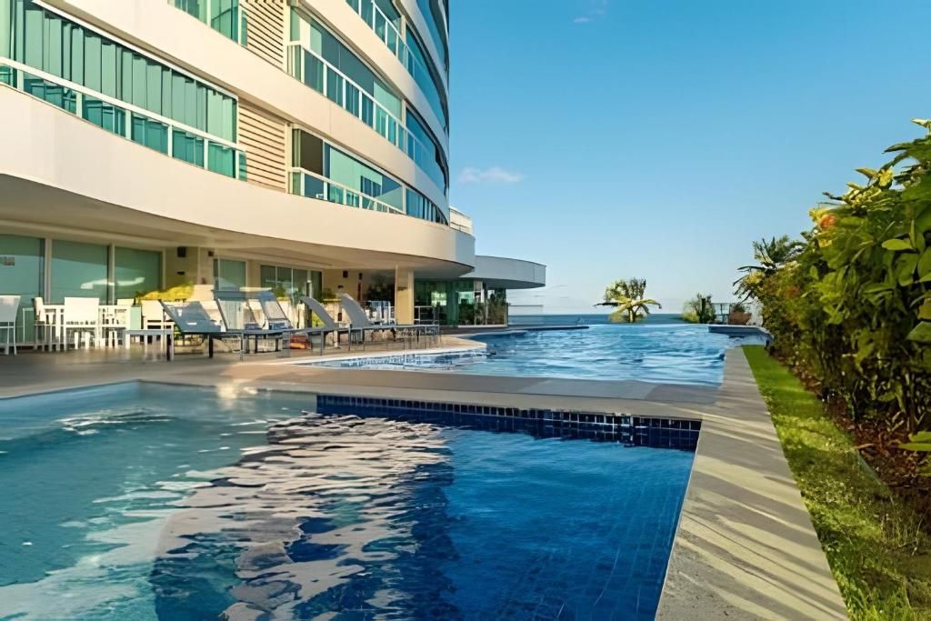 A modern hotel with a swimming pool, lounge chairs, and a view of the ocean.