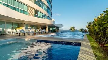 A modern hotel with a swimming pool, lounge chairs, and a view of the ocean.