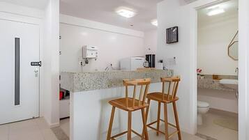 Cozinha moderna com bancada de granito, dois banquetes de madeira, cafeteira e geladeira.