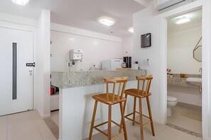 Una cocina moderna con encimera de granito, dos taburetes de madera, una cafetera y un refrigerador.