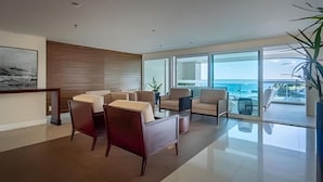 A modern living room with a view of the ocean, featuring a sofa set, a coffee table, and a large window. - Pé de Areia Barra Ondina (Salvador)