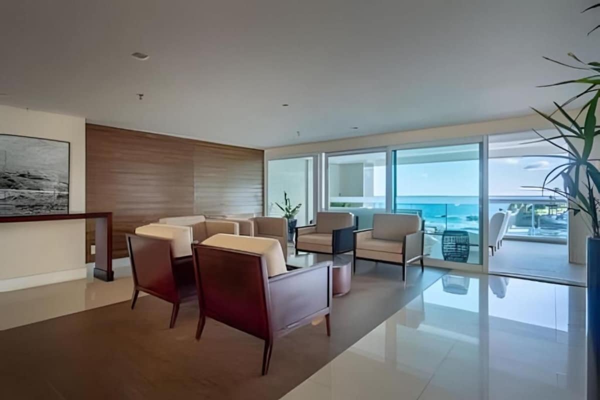 Una sala de estar moderna con vista al océano, que incluye un juego de sofás, una mesa de centro y un ventanal grande.