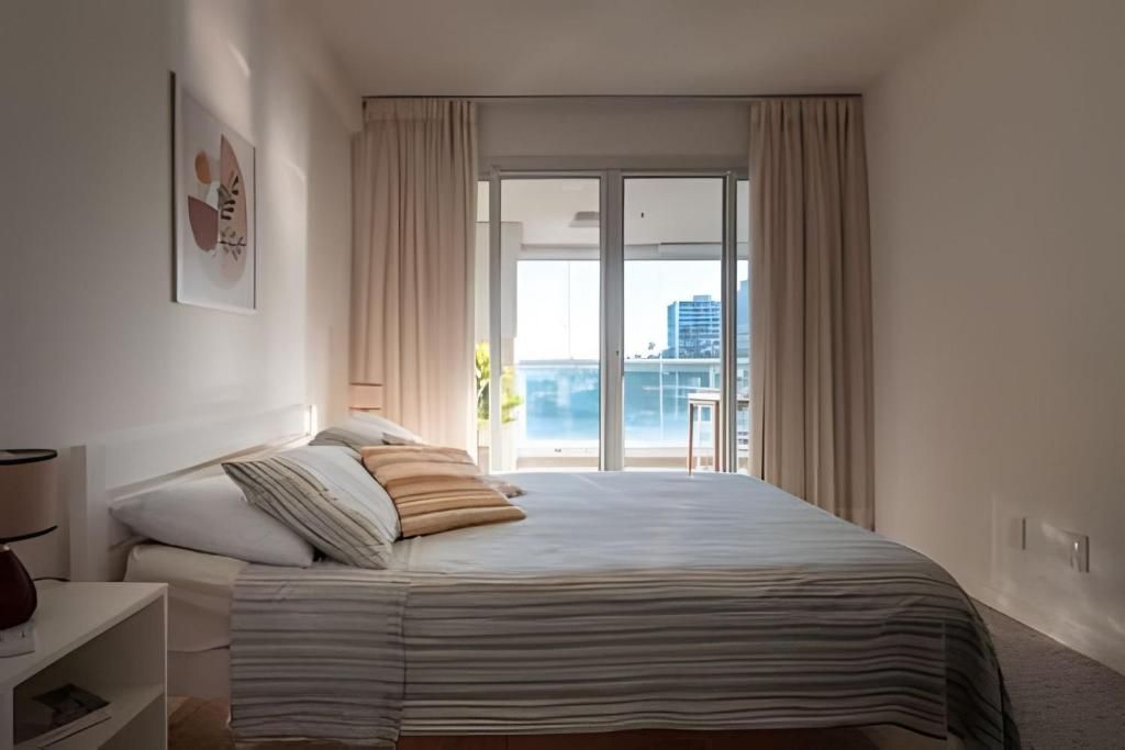 Ein Hotelzimmer mit Bett, Nachttisch, Lampe und einem Fenster mit Vorhängen.