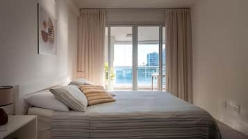 Ein Hotelzimmer mit Bett, Nachttisch, Lampe und einem Fenster mit Vorhängen.