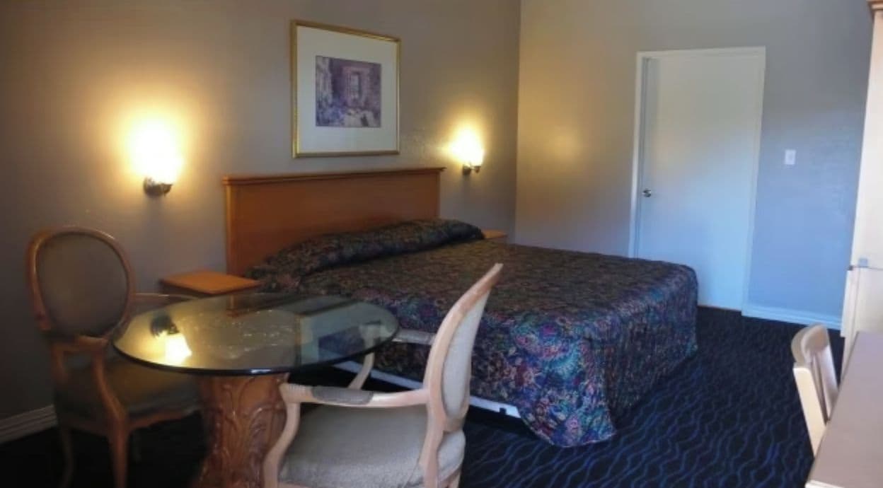 Une chambre d’hôtel avec un lit, une chaise, une table et deux lampes fixées au mur.