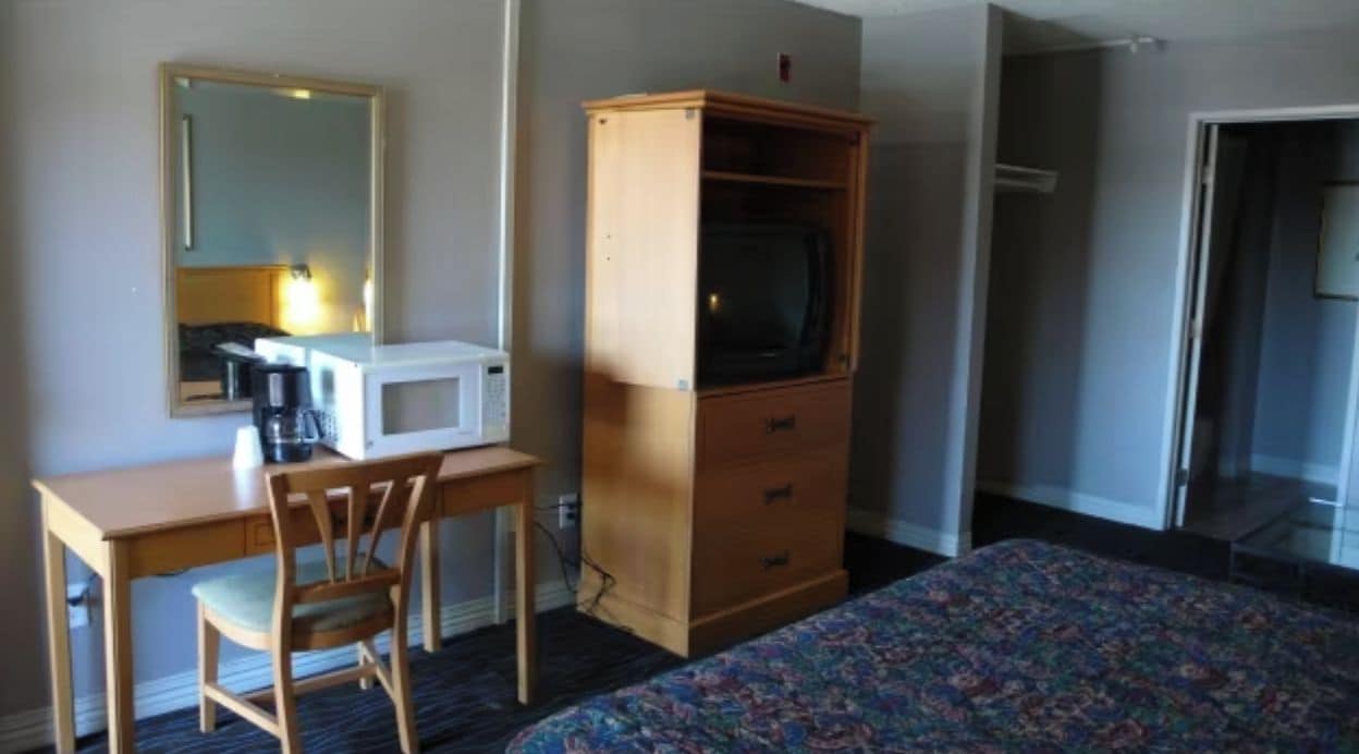 Une chambre d’hôtel comprenant un lit, un bureau avec une chaise, une télévision et une armoire.