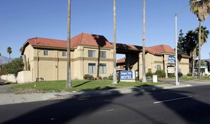 A motel with a red-tiled roof, a covered parking area, and a sign indicating the name 'Pepper Tree Motel.'
