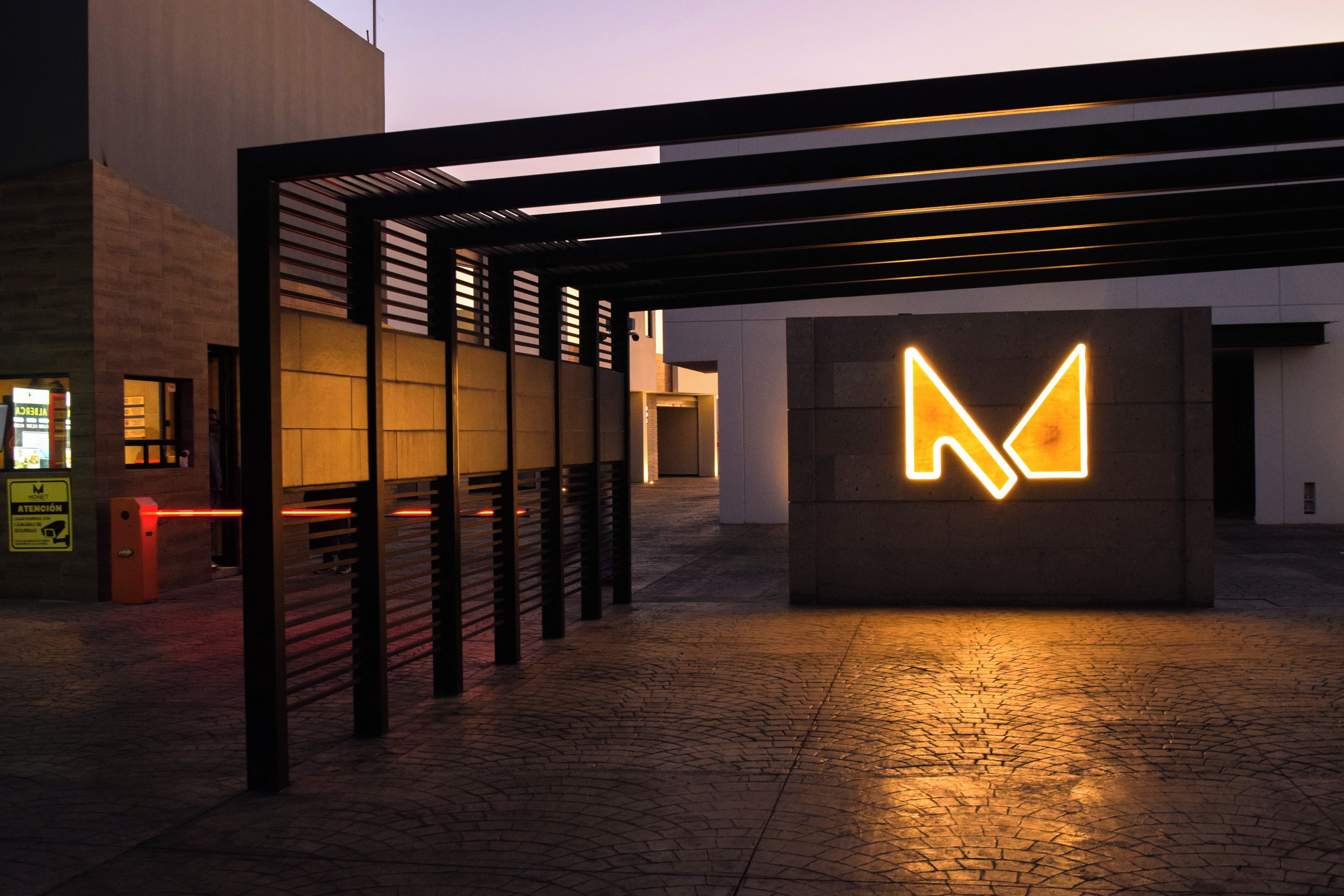 Une entrée moderne avec un grand panneau lumineux en forme de « M », une allée couverte et un trottoir pavé de briques.