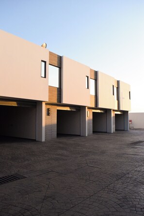 Un edificio moderno con varias puertas de garaje, suelo pavimentado y cielo despejado.