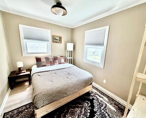 A bedroom with a bed, nightstand, lamp, windows, and a ceiling fan. - King Bed • Vintage Urban Oasis • Near MKE Airport (Milwaukee)