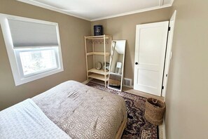 Een slaapkamer met een bed, een raam met zonwering, een kledingkast, een spiegel en een vloerkleed.