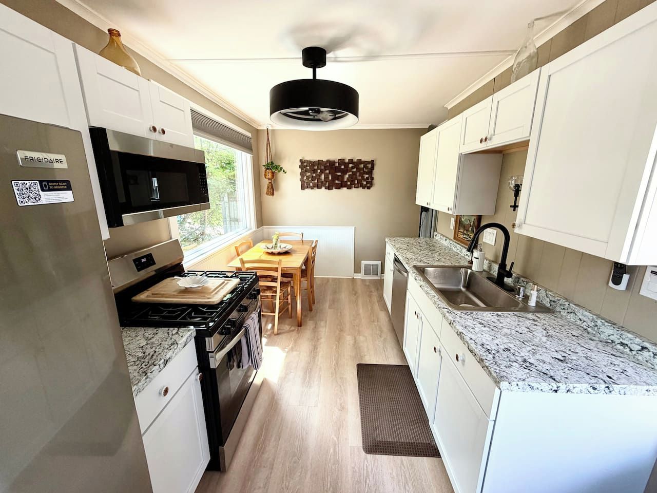 Una cocina compacta con gabinetes blancos, un microondas integrado, una estufa a gas y una encimera de granito.