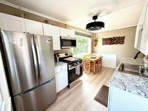 A modern kitchen with stainless steel appliances, a dining area with a wooden table and chairs, and a view of greenery outside. - King Bed • Vintage Urban Oasis • Near MKE Airport (Milwaukee)