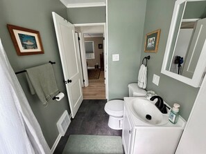 A bathroom with a toilet, sink, and towel rack. There is a door leading to another room. - King Bed • Vintage Urban Oasis • Near MKE Airport (Milwaukee)
