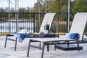 Eine Terrasse mit zwei Liegestühlen, einem Tisch, einem Wasserkocher und einem Hut.