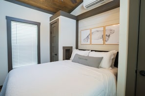 Ein Schlafzimmer mit Bett, Fenster mit Jalousien, einer Tür und einer Wand-Klimaanlage.
