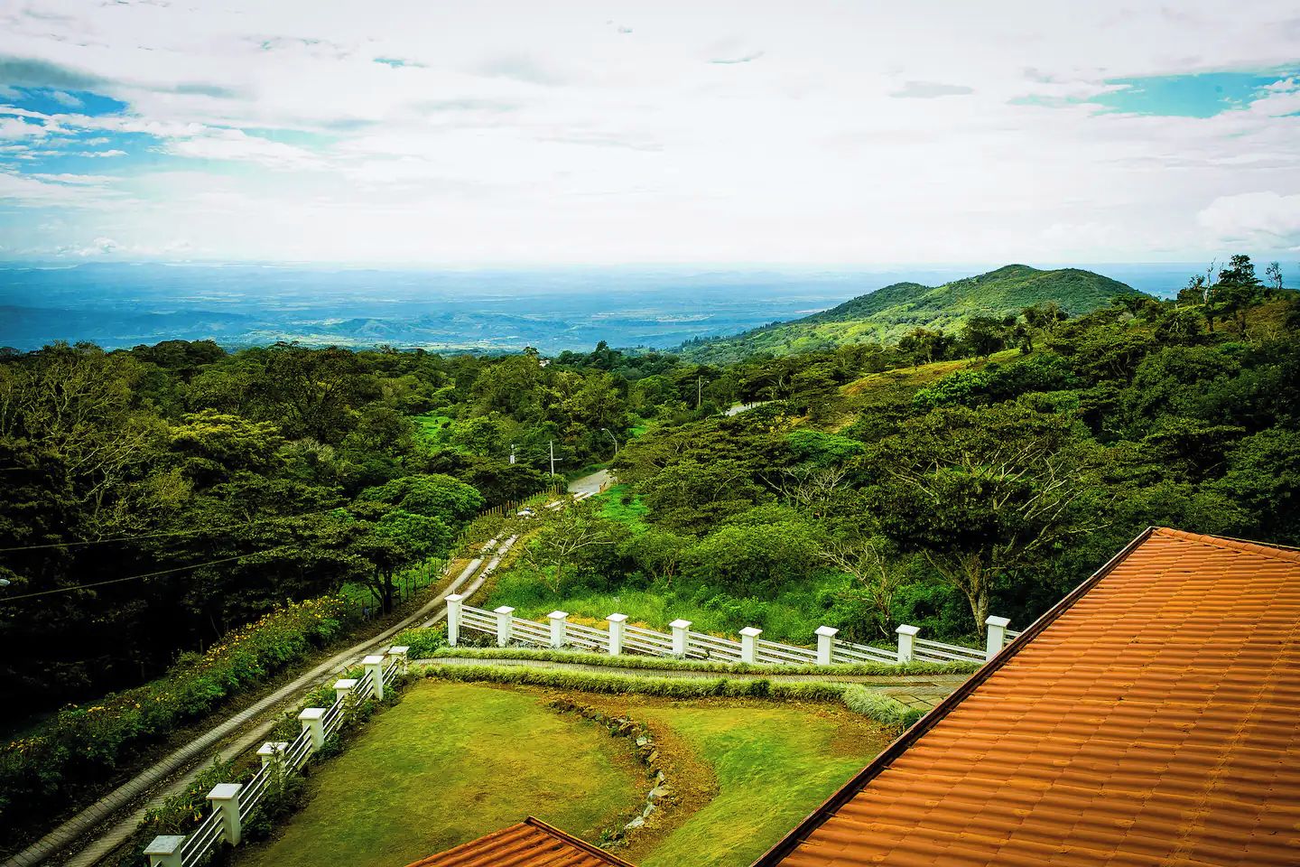 A lush green landscape with a pathway leading to a building with a red roof.