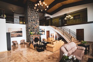 A spacious living area with a stone fireplace, comfortable seating, a staircase, and artwork on the walls. - La Villa Real — Tu sueño en Boquete.
La Villa Real — Your dream in Boquete. (Jaramillo)
