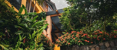 A stone staircase leading to a building with a yellow facade, surrounded by lush greenery and flowering plants.
