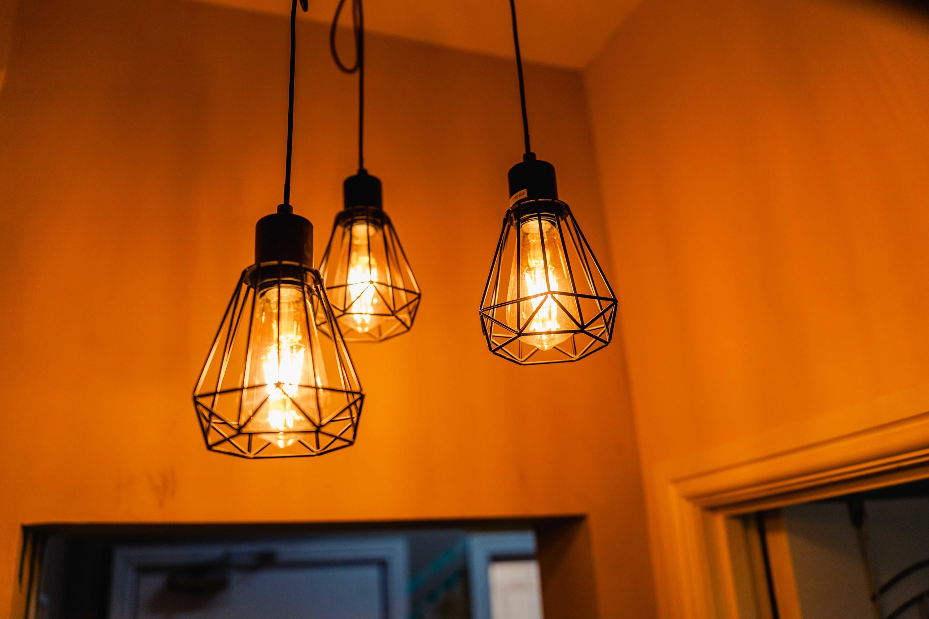 Three hanging light fixtures with a geometric design against a warm wall.