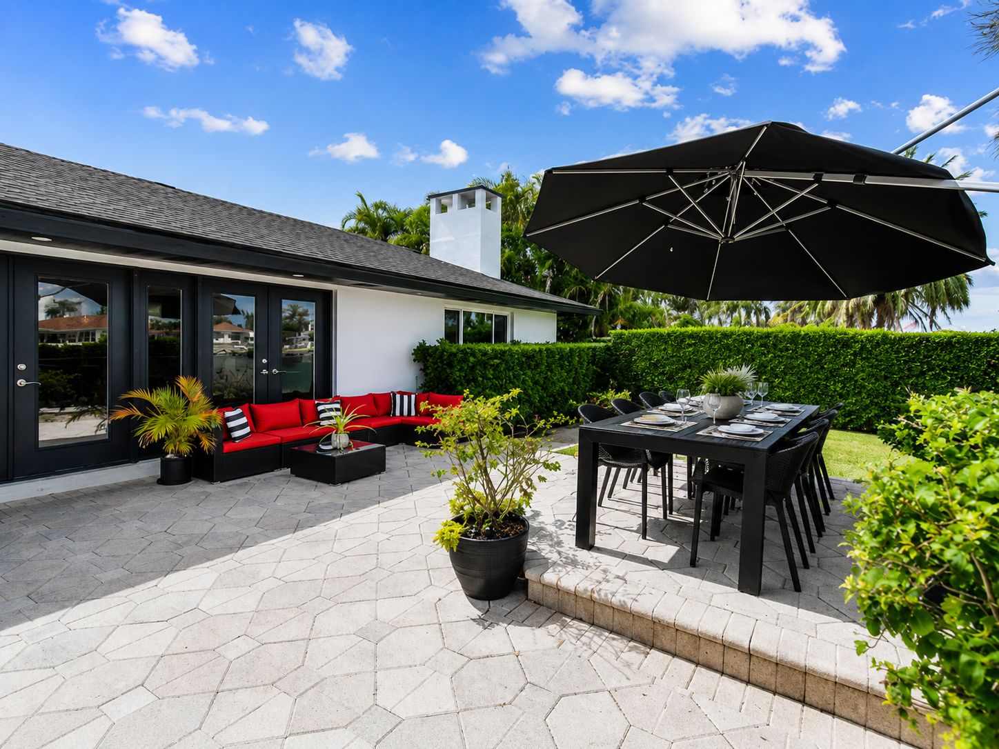 Une terrasse extérieure moderne, agrémentée d’un parasol noir, d’un canapé rouge et d’une table à manger pour quatre personnes.