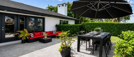 A modern outdoor patio with a black umbrella, a red sofa, and a dining table set for four.