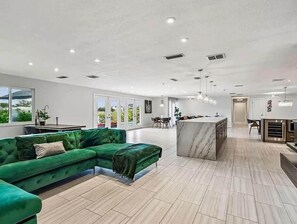 A spacious living area with a green sectional sofa, a marble island, and a kitchen area with modern appliances. - Belleair Beach Waterfront Residence (Belleair Beach)