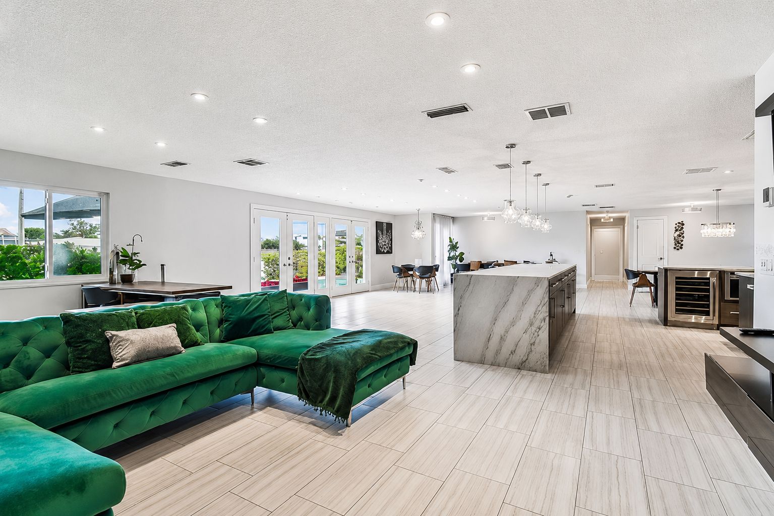 A modern living room with a green sectional sofa, a marble island, and a kitchen in the background.