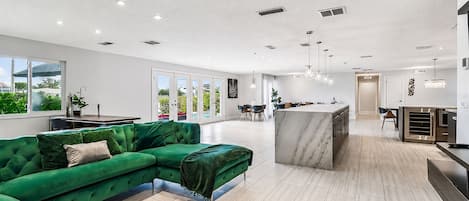 A modern living room with a green sectional sofa, a marble island, and a kitchen in the background.