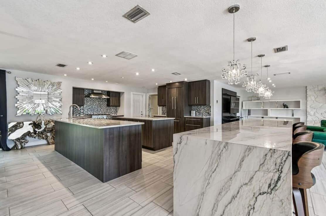 A modern kitchen with a marble island, dark wooden cabinets, and pendant lighting.