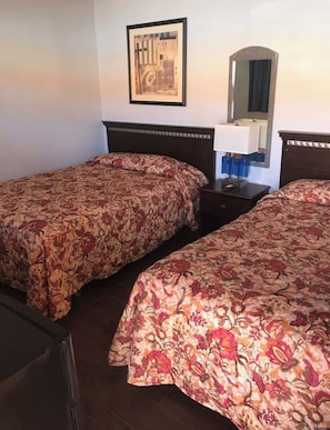 A hotel room with two single beds, a nightstand with a lamp, a mirror, and a framed picture on the wall. - Tradewinds Motel (Homestead)