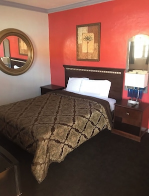 A hotel room with a bed, a nightstand, a mirror, and a painting on the wall. - Tradewinds Motel (Homestead)