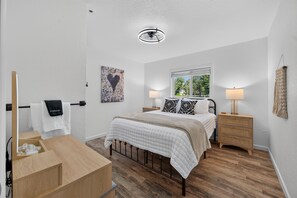 Une chambre à coucher avec un lit, des tables de chevet, une fenêtre et un luminaire au plafond.