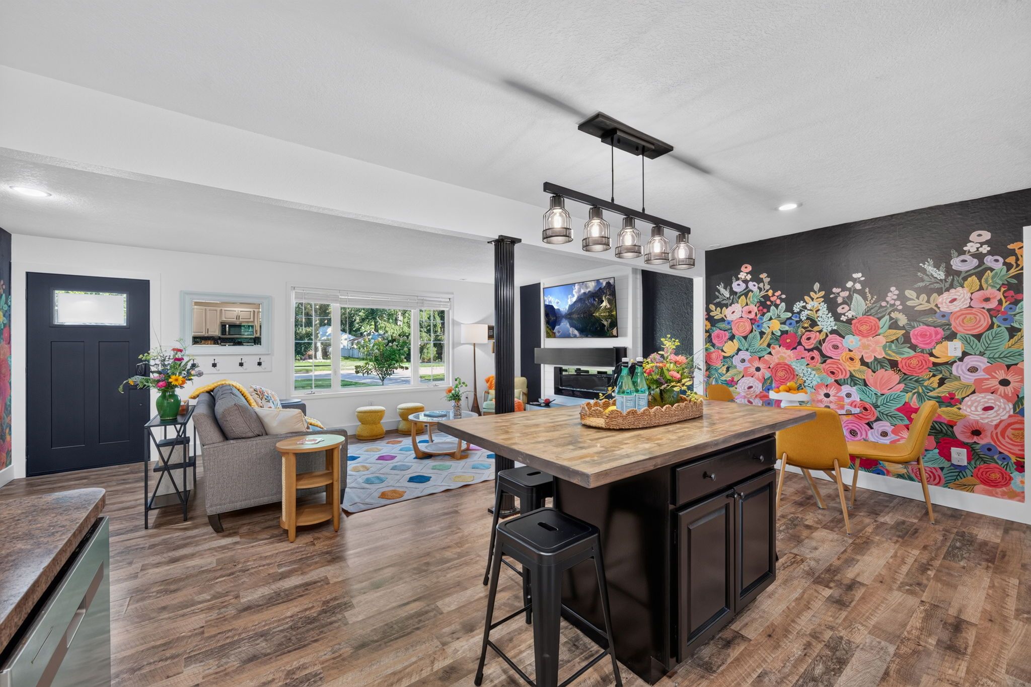 A modern kitchen with a central island, bar stools, and a dining area with a colorful floral mural.